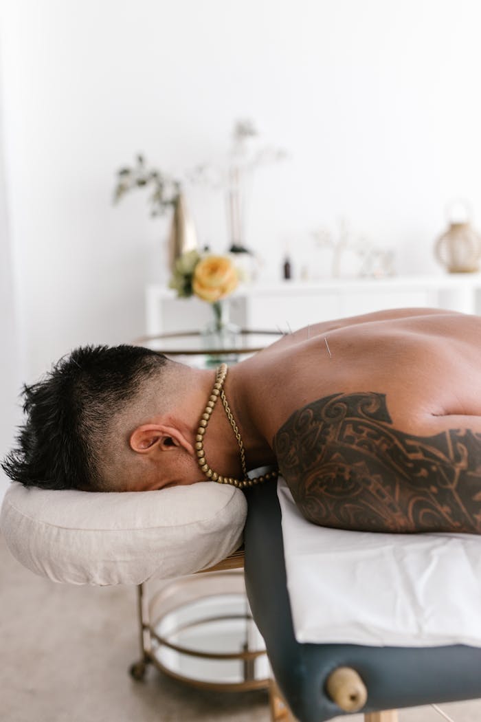 about-us-02 Tattooed man lying face down on a massage table in a spa setting for relaxation and wellness.